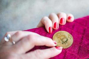 dinero virtual bitcoin dorado en monedero de tela de mujer rosa. dedos con uñas rojas en una moneda foto