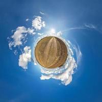 green tiny planet in blue sky with sun and beautiful clouds. Transformation of spherical panorama 360 degrees. Spherical abstract aerial view. Curvature of space. photo