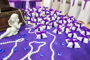 ángel de cerámica sobre la mesa con un mantel violeta y pequeños obsequios para los invitados de los recién casados foto