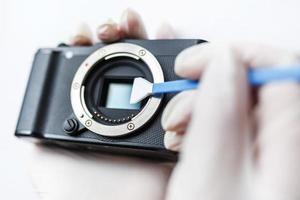 Close-up of mirrorless digital APS-C dirty camera matrix sensor cleaning and maintenance with swab, photographer cleaning photocamera on white background photo