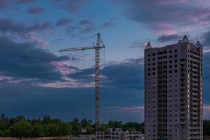 grúas de torre y altura de varios pisos sin terminar cerca de edificios en construcción por la noche foto