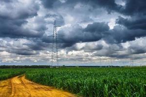 silueta de las torres de pilón eléctrico de alto voltaje en el fondo de hermosas nubes de tormenta cerca de la carretera de arena amarilla foto