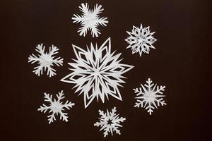 White paper snowflakes different shapes and sizes on brown cardboard background. Top view. photo