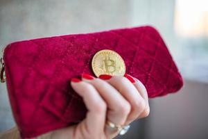 dinero virtual bitcoin dorado en monedero de tela de mujer rosa. dedos con uñas rojas en una moneda foto