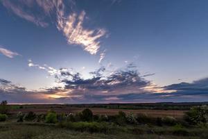 Blue red sky background with evening fluffy curly rolling clouds with setting sun. Good windy weather photo