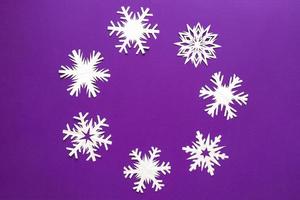 copos de nieve de papel blanco de diferentes formas y tamaños sobre fondo violeta. vista superior. foto