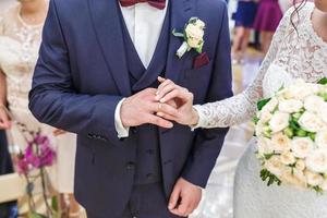 groom embraces the bride with wedding bouquet with violet rose . groom dresses an engagement ring to the bride. newlyweds exchange wedding rings photo