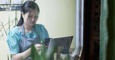 Restaurant manager surfing the web and conversing on her smartphone at coffee shop viewed through glass with reflections. video