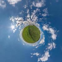 green tiny planet in blue sky with beautiful clouds. Transformation of spherical panorama 360 degrees. Spherical abstract aerial view. Curvature of space. photo