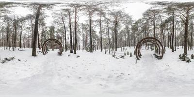 Winter full spherical seamless panorama 360 degrees angle view on road in a snowy park with gray pale sky near arches and benches in equirectangular projection. VR AR content photo