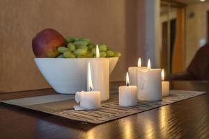 burning candles and a vase with fruit apples and grapes on the table near the lamp photo