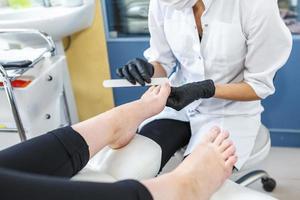 el maestro de guantes negros en el salón hace manicura pedicura al cliente foto