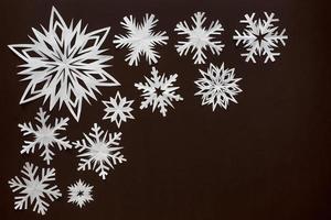 White paper snowflakes different shapes and sizes on brown cardboard background. Top view. photo