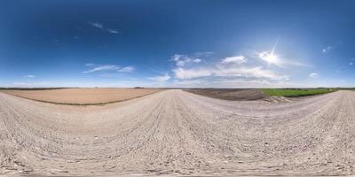 panorama hdr esférico completo sin costuras vista en ángulo de 360 grados en camino de grava de arena blanca entre campos en primavera con nubes impresionantes en proyección equirectangular, listo para contenido de realidad virtual vr foto