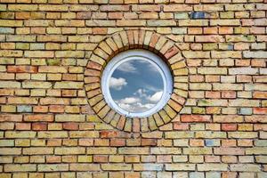 sky with clouds reflected in a round window on brick wall photo