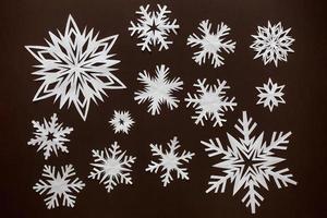 White paper snowflakes different shapes and sizes on brown cardboard background. Top view. photo