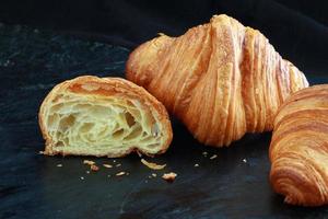 croissant francés, a la mitad, mira la textura, mantecoso fresco sobre fondo oscuro. disparar de cerca foto