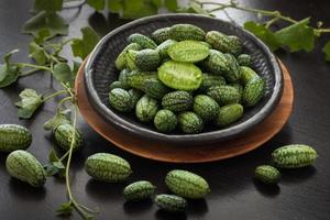 cucamelon también conocido como melothria scabra, pepinillo de pepino agrio mexicano, recién recogido. cerrar en un plato de cerámica, fondo de madera oscura foto