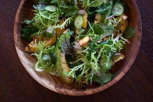Avocado salad in a wooden plate  looking fresh and organic, with some micro edible greens. on the table. Low key lighting, close up and selective focus. Great Image for restaurant menu photo
