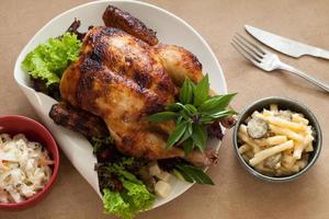 asador de pollo con ensaladas de pasta a los lados, cuchillo y tenedor, primer plano en un plato de cerámica sobre la mesa. vista superior horizontal desde arriba foto