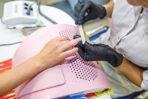 el maestro de guantes negros en el salón hace manicura pedicura al cliente foto