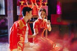 feliz joven pareja asiática con vestidos tradicionales chinos rezando en el templo foto