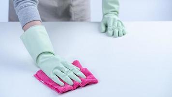 Woman housekeeper wearing protective gloves and using rag to wipe clean the table surface. photo