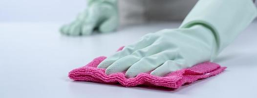 Woman housekeeper wearing protective gloves and using rag to wipe clean the table surface. photo