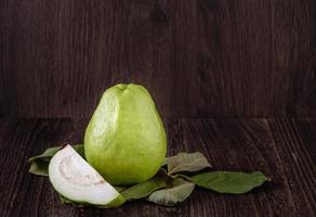 Close up of delicious guava with fresh green leaves on wooden background. photo