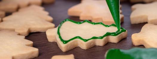 primer plano de dibujo de galletas de azúcar de árbol de Navidad sobre fondo de mesa de madera con glaseado. foto