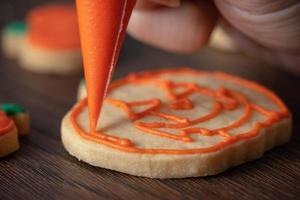 cerca de decorar lindas galletas de calabaza de halloween con glaseado en bolsa de hielo. foto