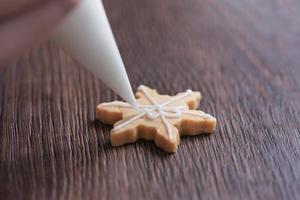 Primer plano de dibujo de galleta de azúcar de copo de nieve de Navidad sobre fondo de mesa de madera con glaseado. foto