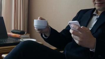 Geschäftsmann, der mit dem Handy arbeitet, während er im Hotelzimmer Kaffee trinkt video