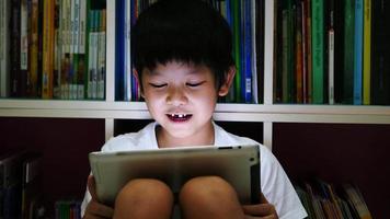 niño asiático de ocho años está jugando tableta en su sala de lectura nocturna oscura video