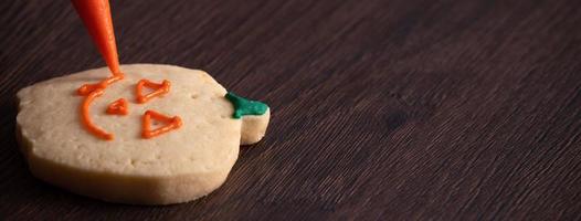 Close up of decorating cute Halloween pumpkin cookies with frosting in icing bag. photo