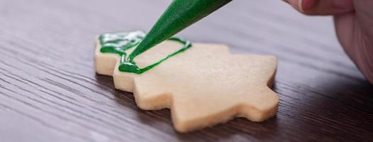 primer plano de dibujo de galletas de azúcar de árbol de Navidad sobre fondo de mesa de madera con glaseado. foto