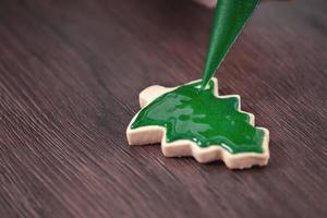 primer plano de dibujo de galletas de azúcar de árbol de Navidad sobre fondo de mesa de madera con glaseado. foto