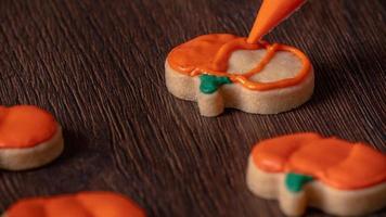 Close up of decorating cute Halloween pumpkin cookies with frosting in icing bag. photo