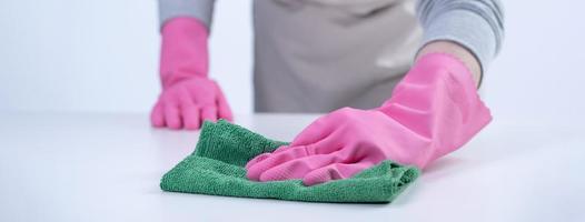 Woman housekeeper wearing protective gloves and using rag to wipe clean the table surface. photo