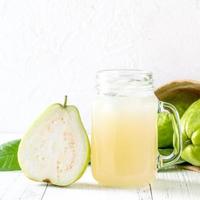 deliciosa fruta de guayaba con jugo fresco sobre fondo de mesa de madera blanca. foto