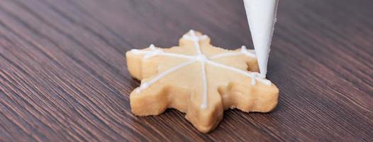 Primer plano de dibujo de galleta de azúcar de copo de nieve de Navidad sobre fondo de mesa de madera con glaseado. foto