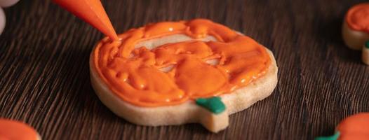 Close up of decorating cute Halloween pumpkin cookies with frosting in icing bag. photo