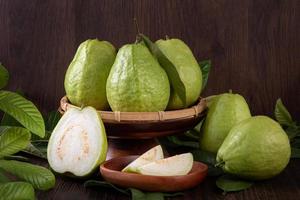 Close up of delicious guava with fresh green leaves on wooden background. photo