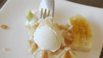usando garfo para comer waffles croffle no prato com sorvete e banana caramelada. video