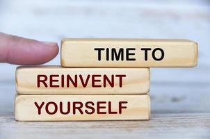 Finger pushing wooden blocks with text - Time to reinvent yourself. photo