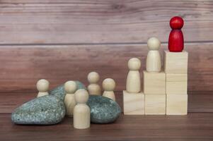 Red wooden doll on top of wooden block with others having to face challenges along the way. photo