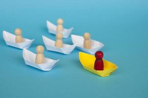 Leadership Concept - Wooden figure on yellow paper ship origami leading the rest of the figure on white paper ship. photo