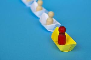 concepto de liderazgo: figura de madera roja en un barco de papel amarillo origami que conduce al resto de la figura en un barco de papel blanco. foto