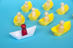 Leadership Concept - Wooden figure on white paper ship origami leading the rest of the figure on yellow paper ship. photo