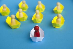 Leadership Concept - Wooden figure on white paper ship origami leading the rest of the figure on yellow paper ship. photo